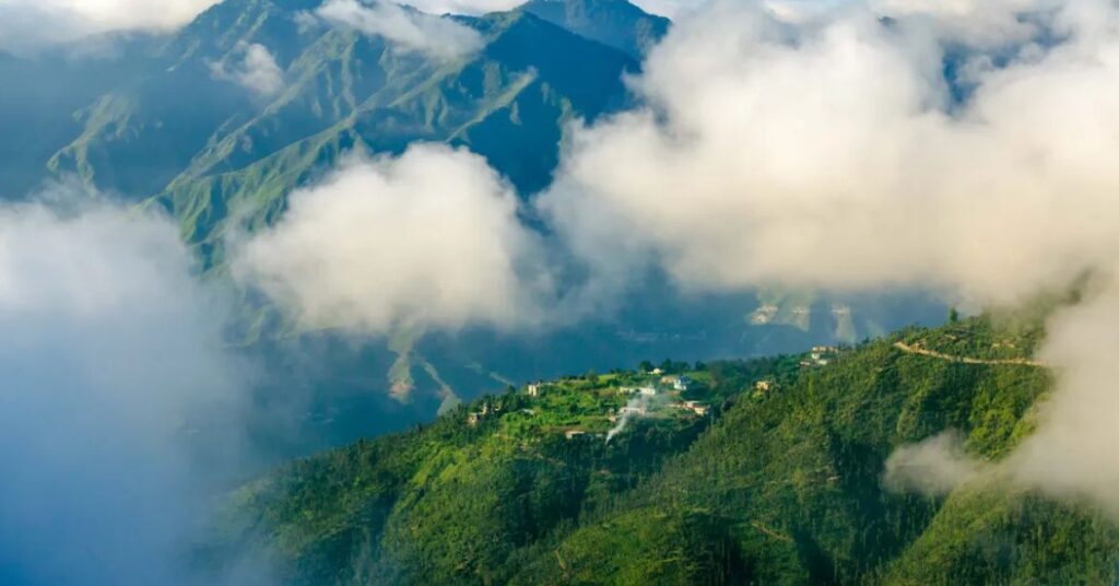 "Mussoorie in the rain with misty clouds drifting over lush green valleys – a serene monsoon landscape in the Himalayas."